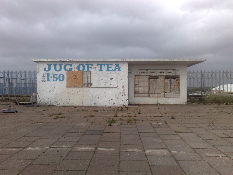 A closed and dilapidated sea-front cafe with 'Jug of Tea' written on it