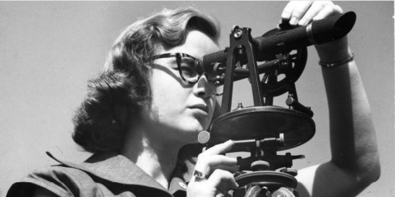 Black and white photo of woman looking through a telescope