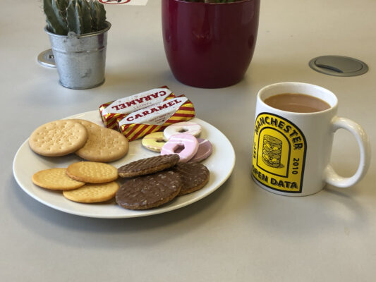 A plate of biscuits and a mug of tea on a desk.