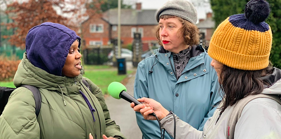 A white woman with a microphone interviewing a black woman outside.