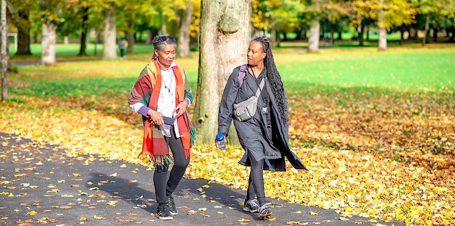 Two black women of different ages talking and walking through a park with leaves on the ground