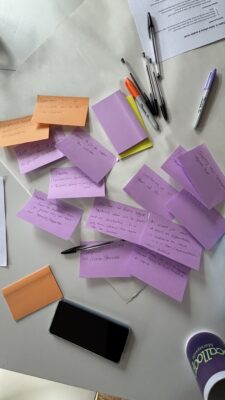 Purple and orange sticky notes scattered on a white surface containing handwritten ideas about data sharing, sectoral barriers, governance challenges, and collaboration opportunities identified during the cross-sector collaboration workshop discussion.