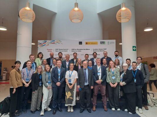 Group shot of UK delegation at OGP Summit 2025 with people lined up against a OGP background board